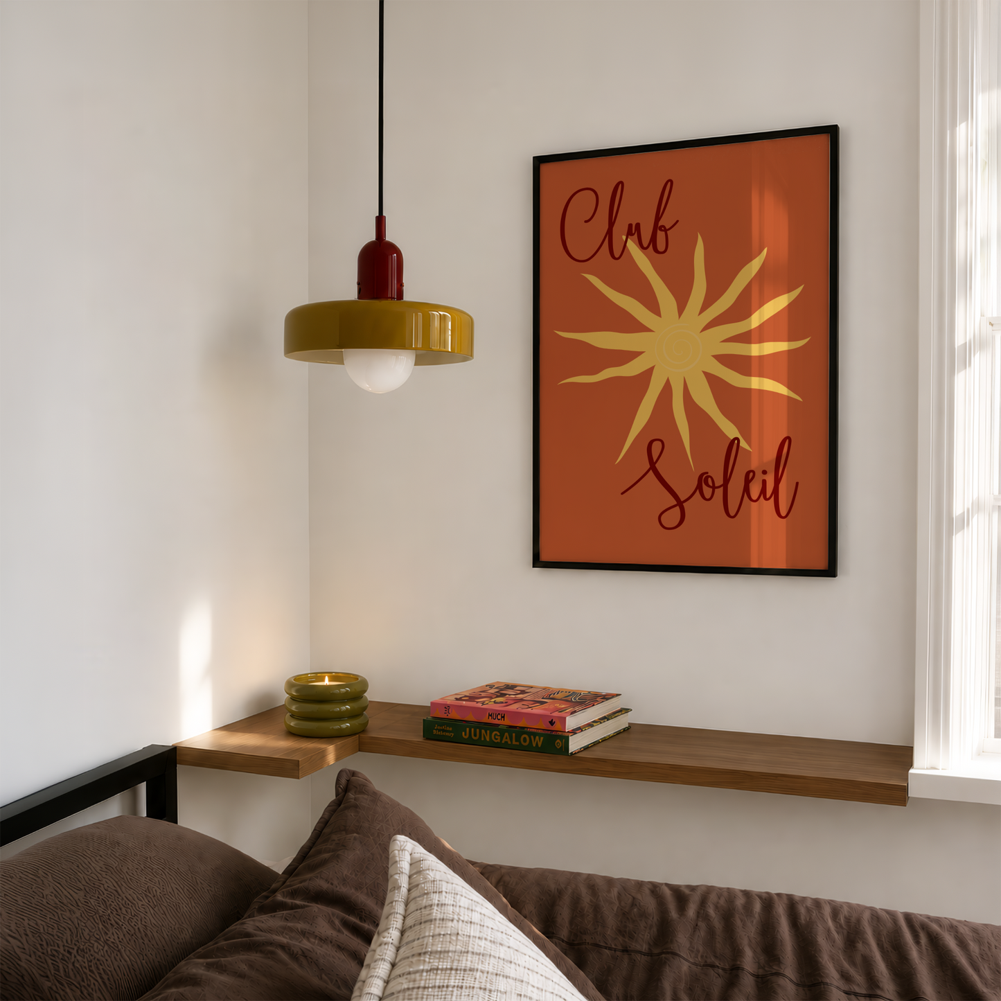 A framed wall art print featuring a retro orange background, a yellow sunburst, and the words 'Club Soleil' in dark script, hanging above a wooden shelf in a modern room setting.