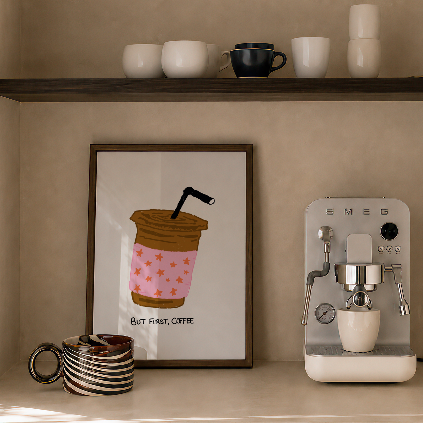 A styled coffee corner with a framed coffee cup illustration on the wall, a countertop espresso machine, stacked ceramic cups on a shelf, and a candle.
