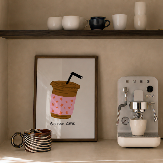 A styled coffee corner with a framed coffee cup illustration on the wall, a countertop espresso machine, stacked ceramic cups on a shelf, and a candle.