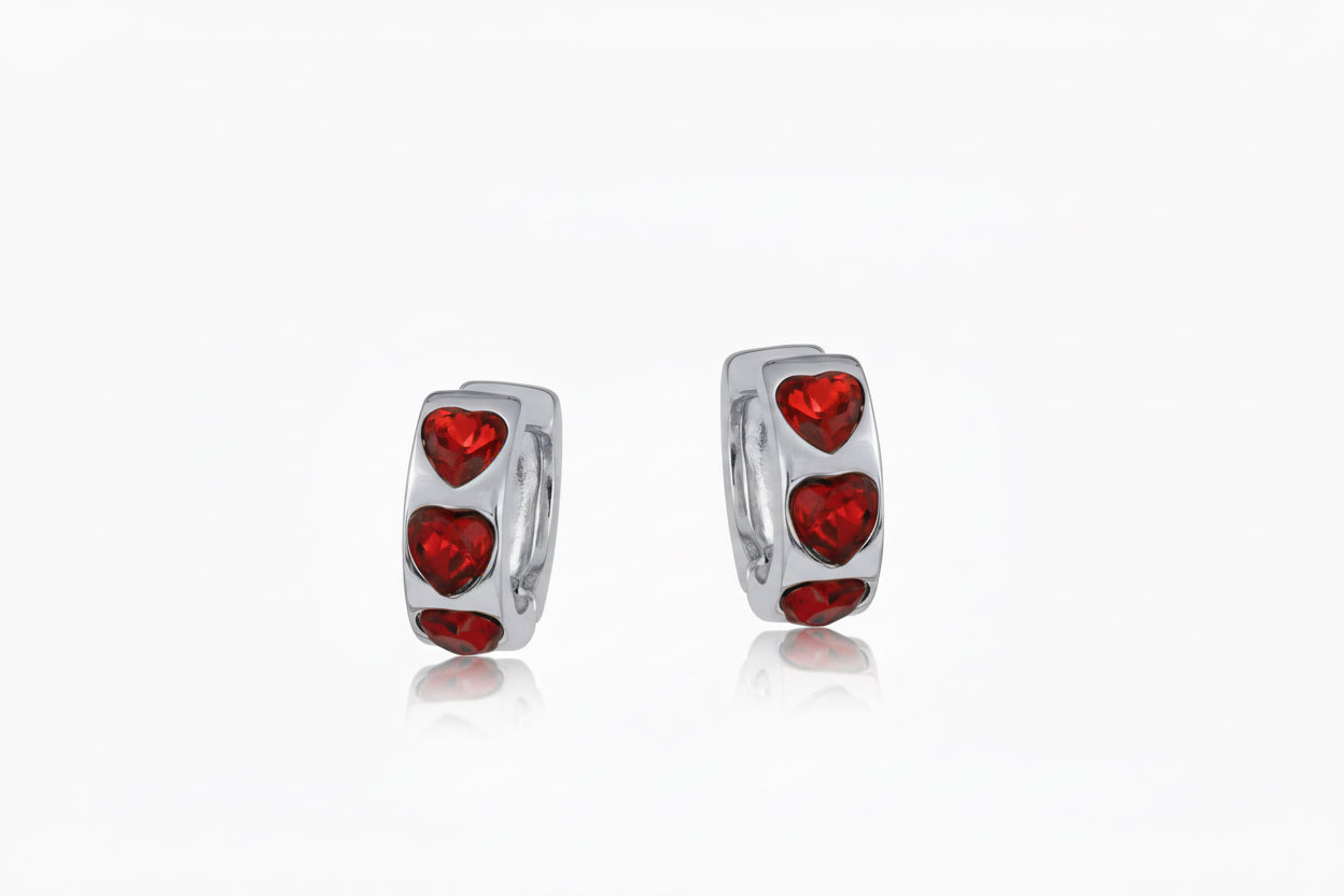 Silver hoop earrings with red heart-shaped stones on a white background