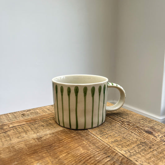 White mug with green patterns on a wooden surface against a plain wall