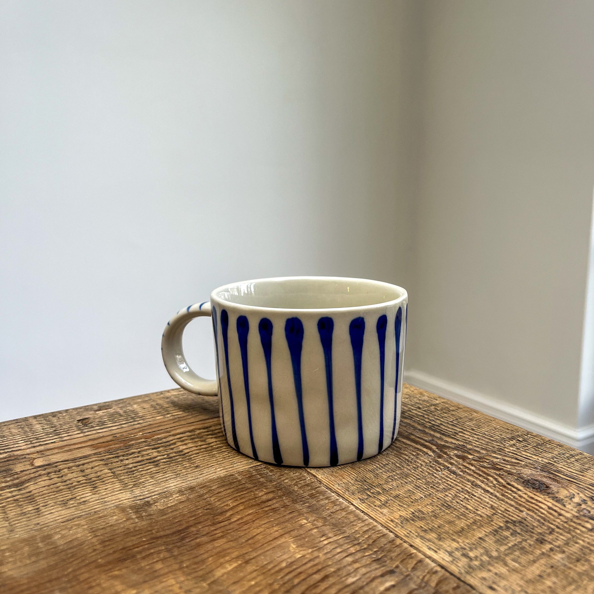 White mug with blue patterns on a wooden surface against a plain wall