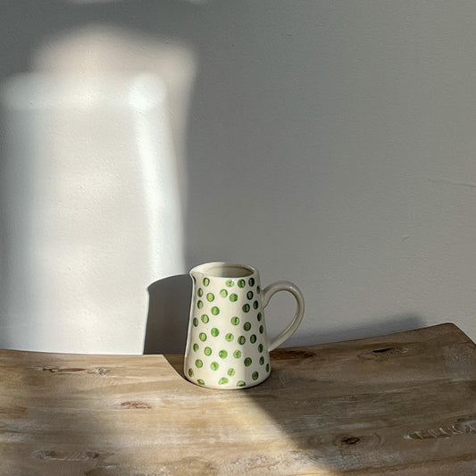 Small green and white polka dot pitcher on a wooden surface with a neutral background