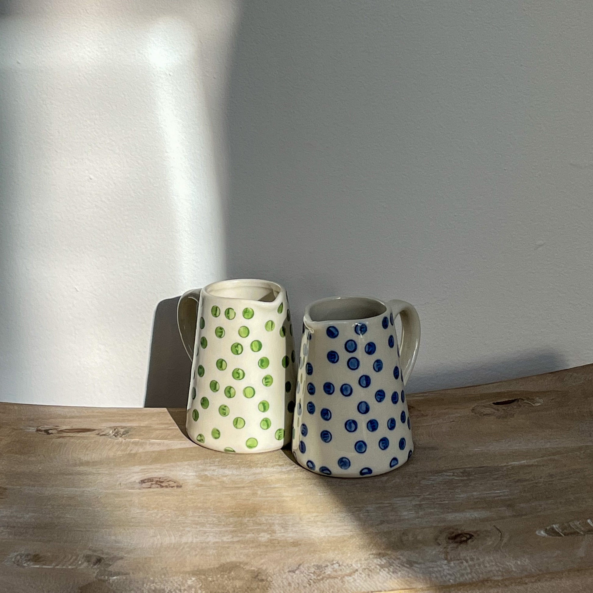 Two ceramic mugs with polka dot patterns on a wooden surface.