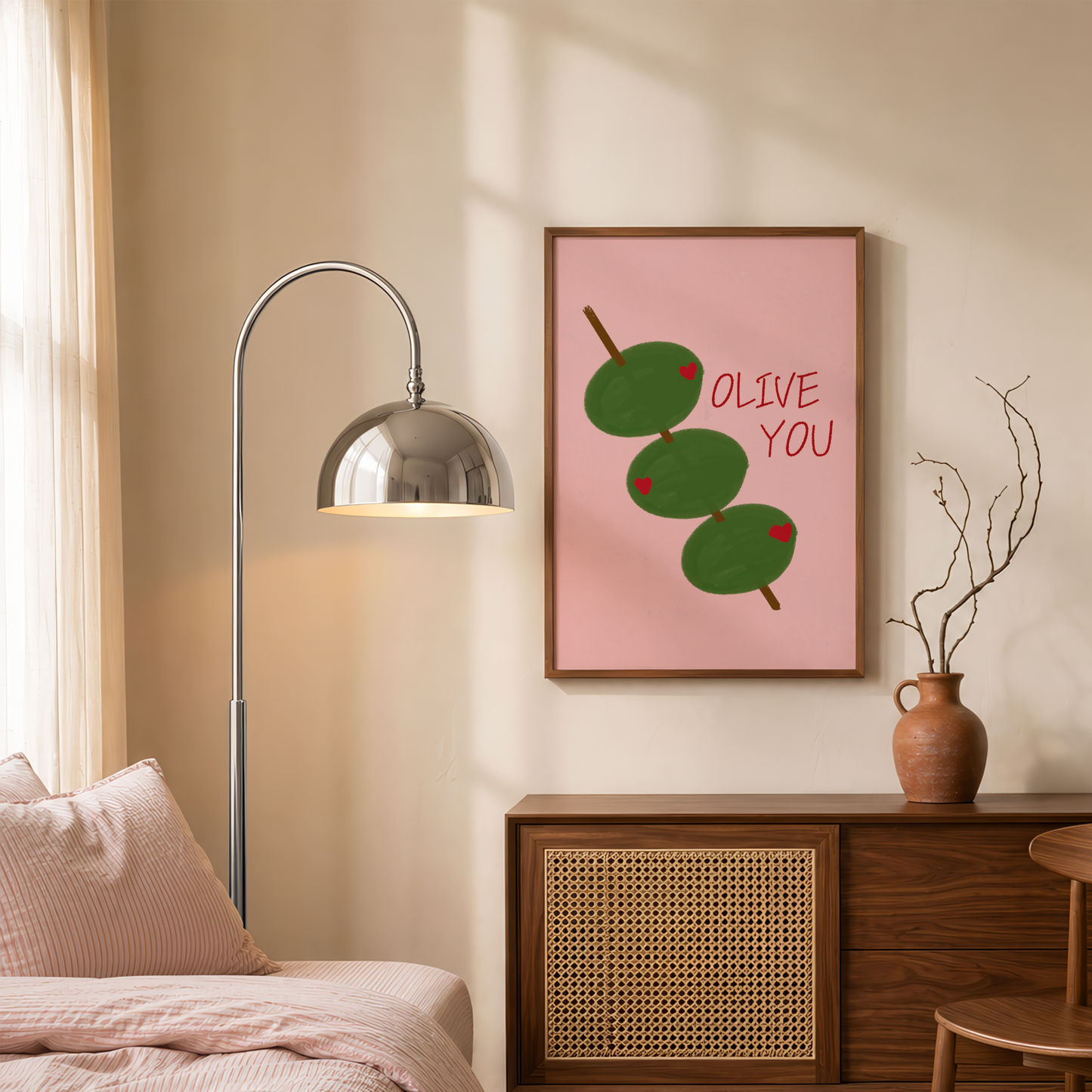 A framed wall art print featuring three green olives on a pink background with the words 'OLIVE YOU' in red, displayed above a wooden sideboard in a styled bedroom setting.