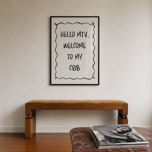A framed typographic wall print reading “HELLO MTV, WELCOME TO MY CRIB” hangs on a light neutral wall above a wooden bench, with a stack of vinyl records on a table in the foreground.